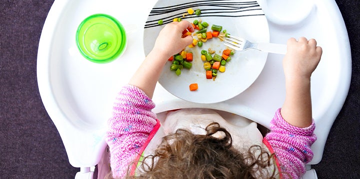 baby in highchair playing with peas corn and carrot on their plate