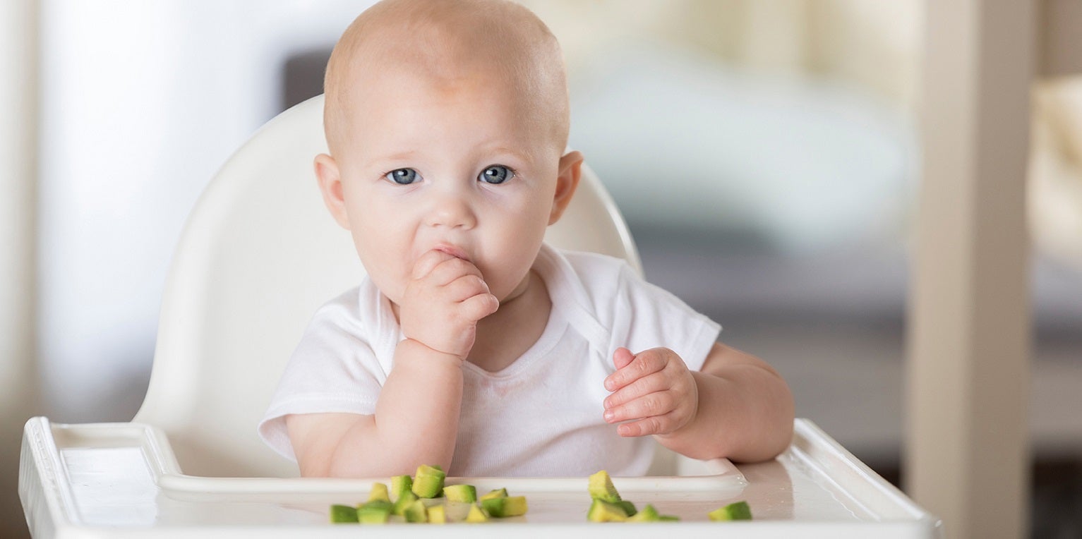 baby eating chopped avocado off their highchair