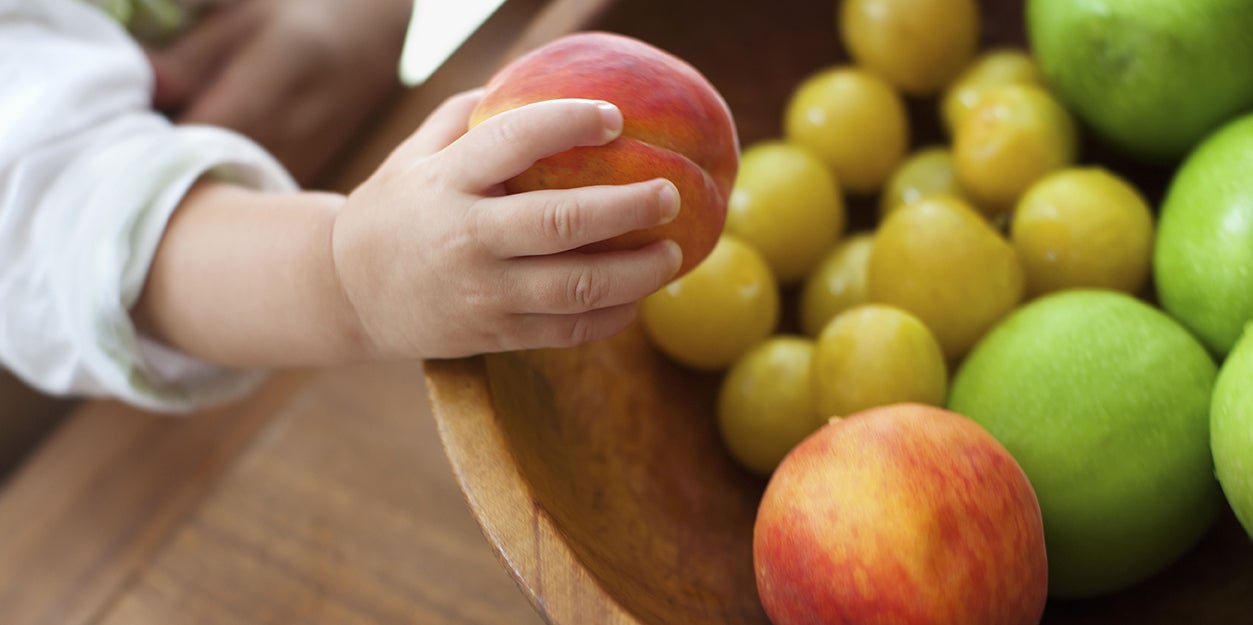 baby taking a nectarine from a fruit bowl