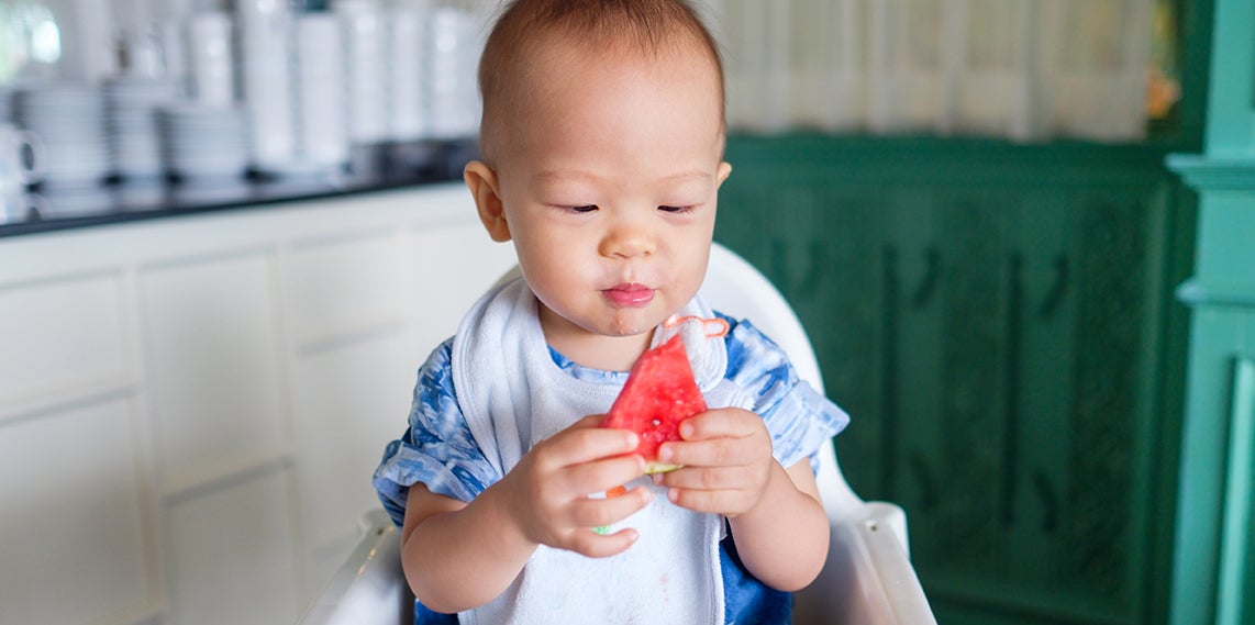 baby eating a slice of watermelon in their highchair