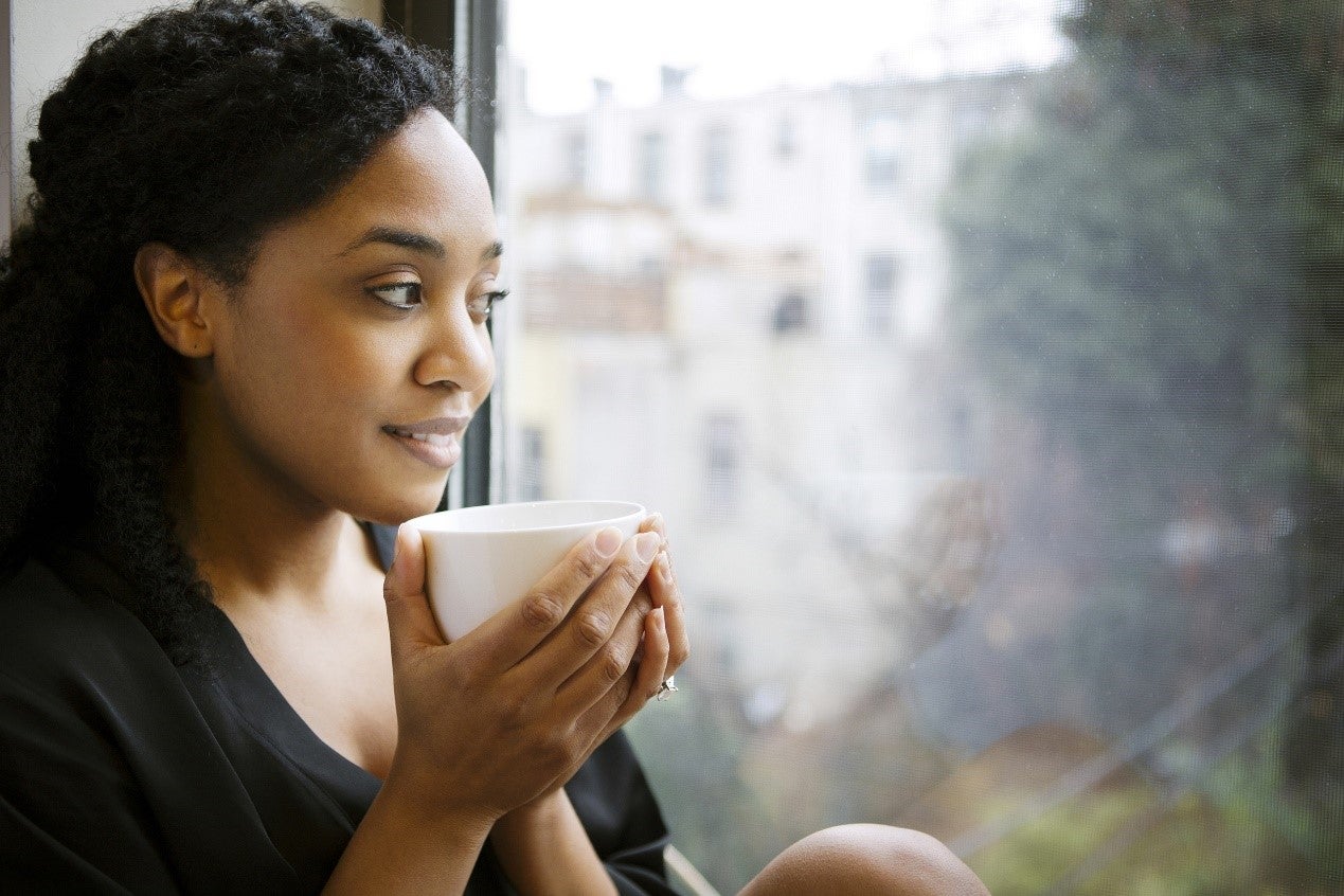 woman drinking out of mug and looking out of a window