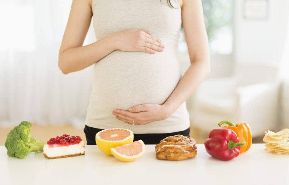 pregnant woman standing over different types of food