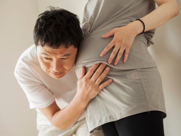 man with ear against pregnant woman's stomach