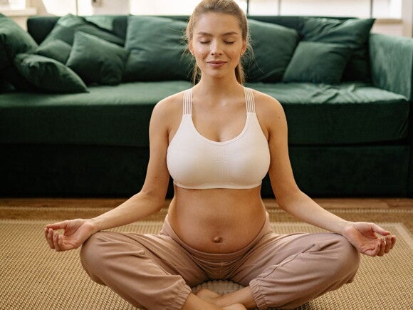 Pregnant woman meditating in a white crop and brown pants