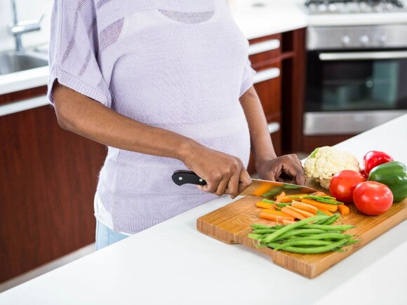 Pregnant woman wearing a purple top chopping vegetables