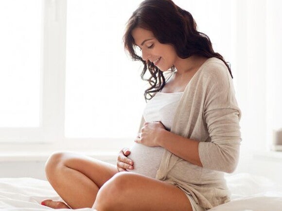 Pregnant woman in white top and cardigan holding her pregnancy belly