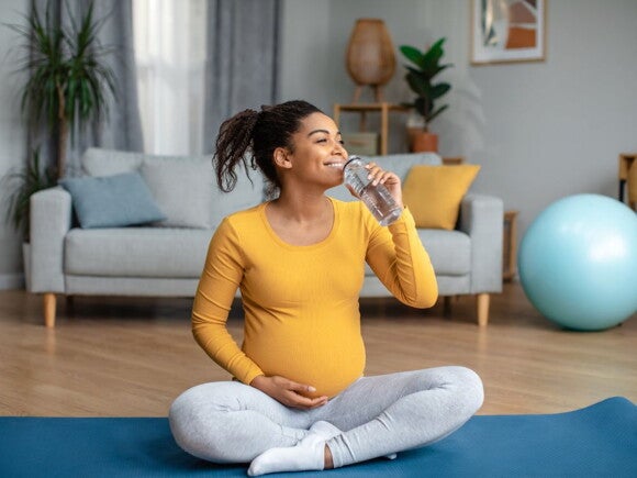 Pregnant woman sitting on a yoga mat drinking water