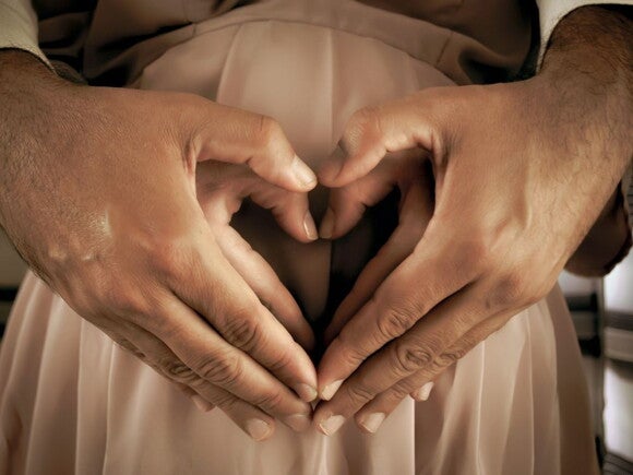 Couple holding hands in the shape of a heart over a pregnant belly