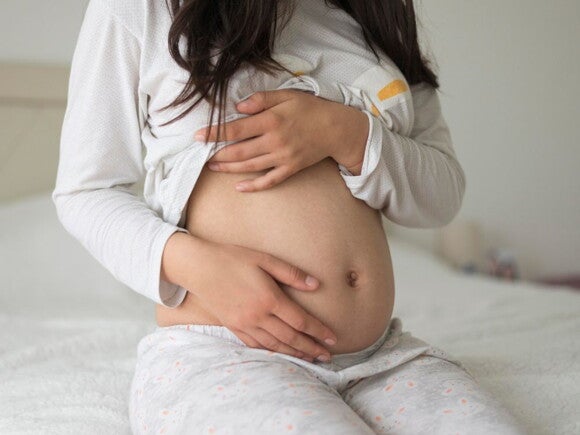 Pregnant woman wearing grey holding her belly
