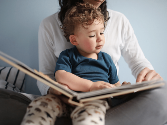 Toddler reading a book on mums lap