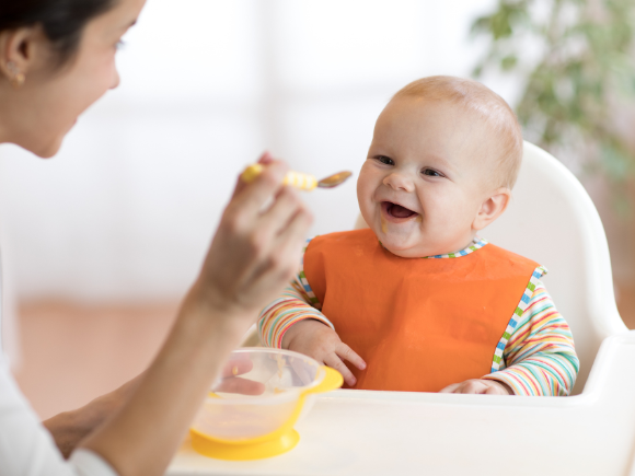 Mother feeding happy baby puree on a spoon