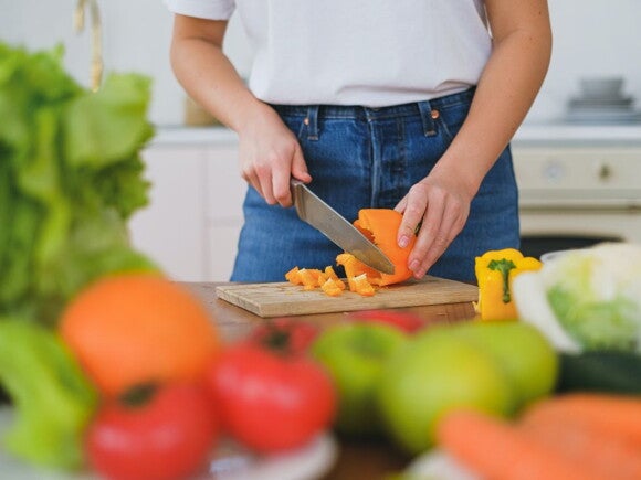 Woman chopping up capsicum on a chopping board with vegetables and fruits around