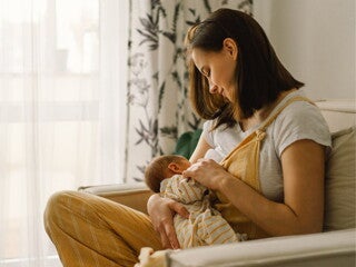 Mother sitting on couch breastfeeding her infant