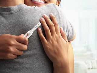 couple hugging with a positive pregnancy test in their hand