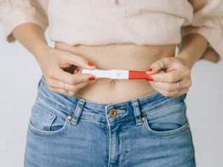 Woman holding a positive pregnancy stick over her stomach