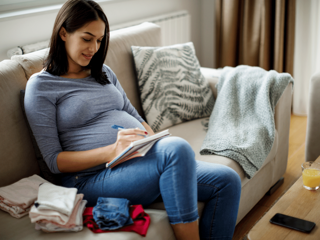 pregnant woman on couch writing on a notepad
