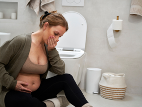 Pregnant lady sitting on the ground in a bathroom with her hand over her mouth