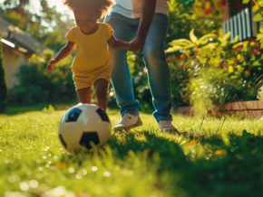 Toddler girl kicking the soccer ball while holding parents hand