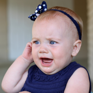 Baby in blue dress crying and pulling on ear