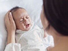 Crying baby in white being comforted by their parent