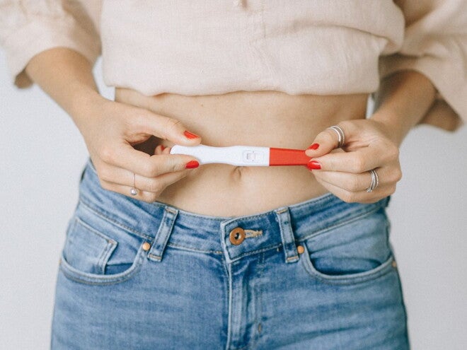 Woman holding a positive pregnancy stick over her stomach