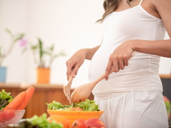 Pregnant woman wearing white clothing tossing salad