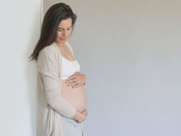 Pregnant woman in grey cardigan and white crop holding her belly