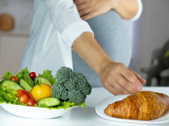 Pregnant woman with a salad and croissant in front of her
