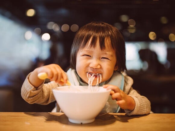 toddler eating noodles from a bowl at a restaurant