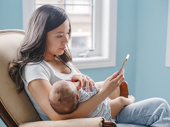 Woman sitting on couch holding her sleeping baby while on the phone