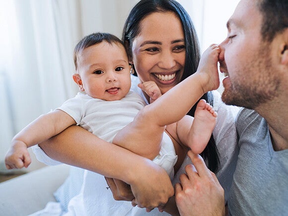 Woman holding her baby while they play with mans face with feet