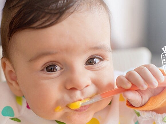 Infant grinning and eating puree.