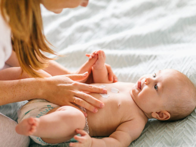 Mother massaging baby laying down with cream