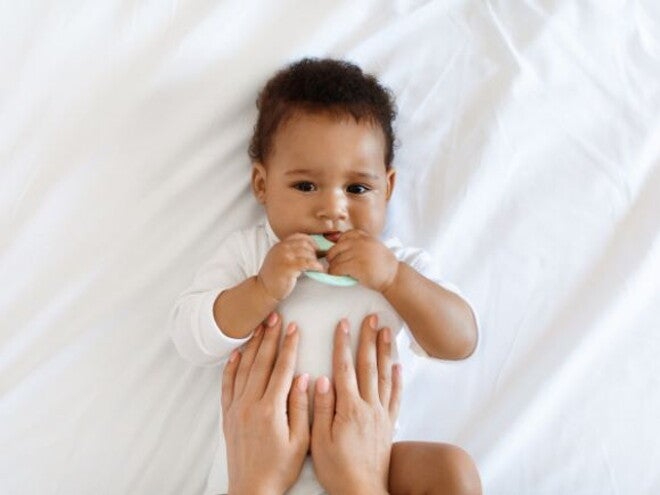 Baby lying down on bed with parents hands rubbing belly