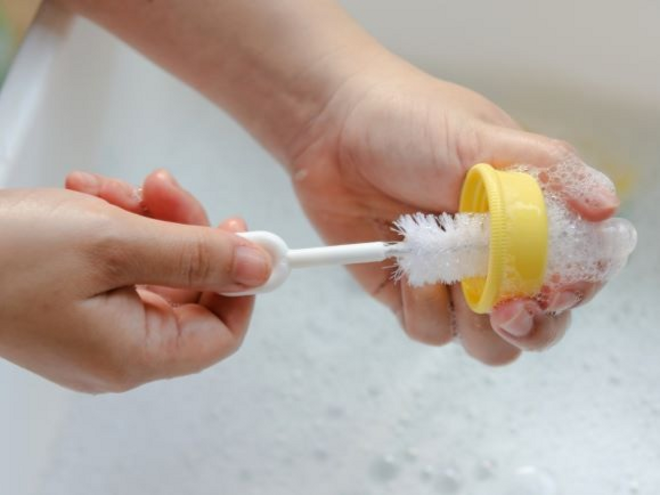 Woman cleaning baby bottle in sink