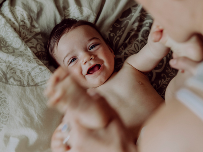 Baby smiling on a bed with his mother