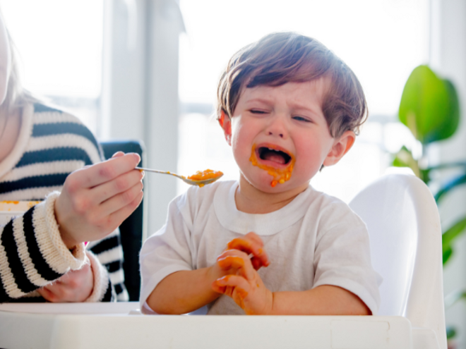 Mother feeding upset toddler boy with spoon