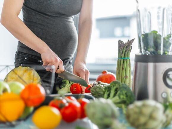 Pregnant woman in dark top cutting vegetables