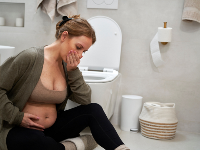 Pregnant lady sitting on the ground in a bathroom with her hand over her mouth