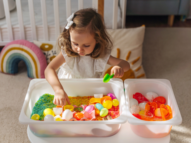 Toddler girl playing with colorful sand and toys