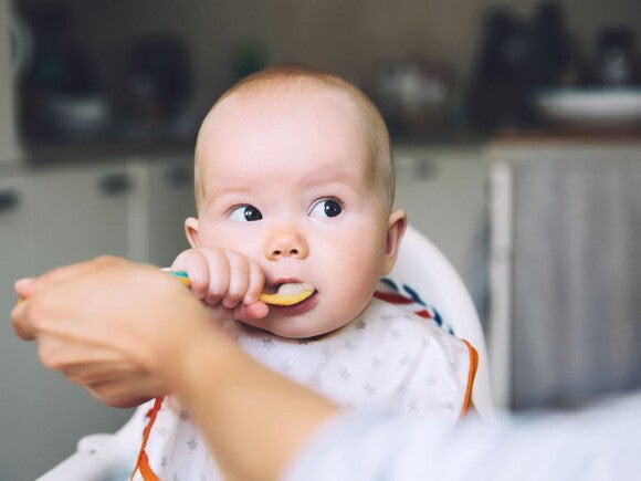 baby eating puree off a spoon in highchair with parents help