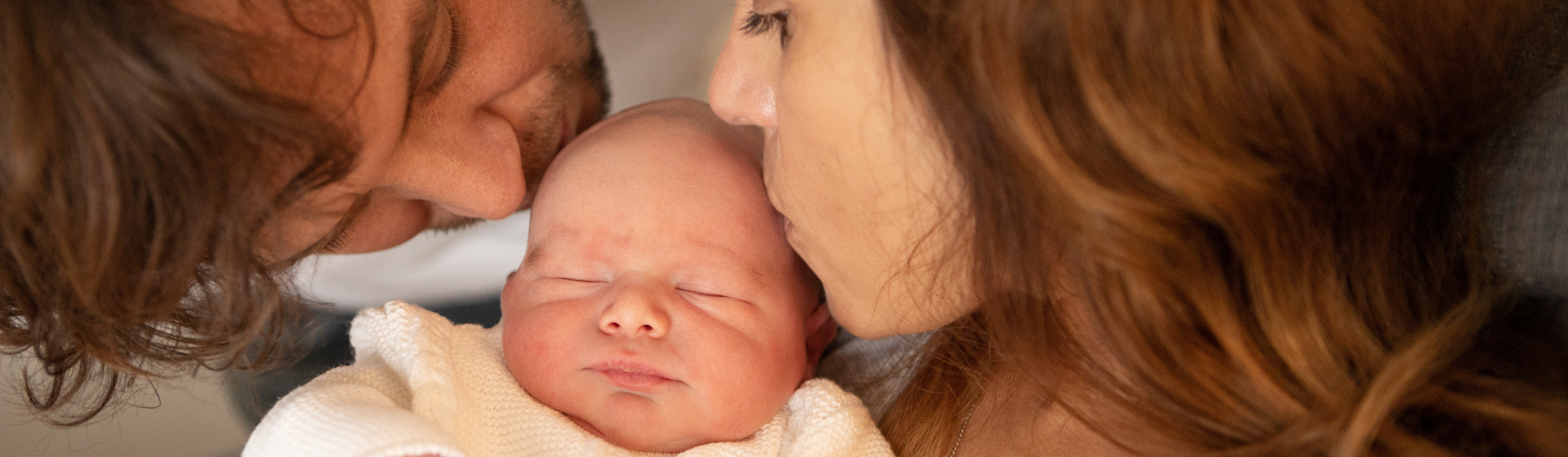 mother and father kissing their newborn baby