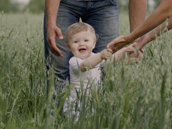 baby holding hands with woman and walking through tall grass