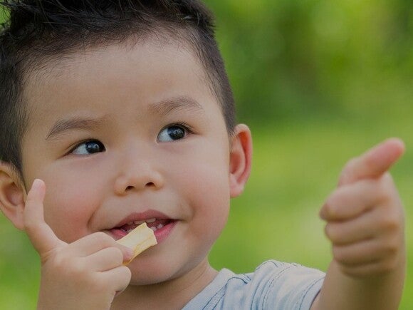 toddler eating a snack and giving thumbs up