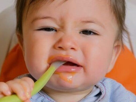 Baby with spoon in mouth looking unimpressed