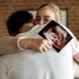 couple hugging holding a scan of their baby